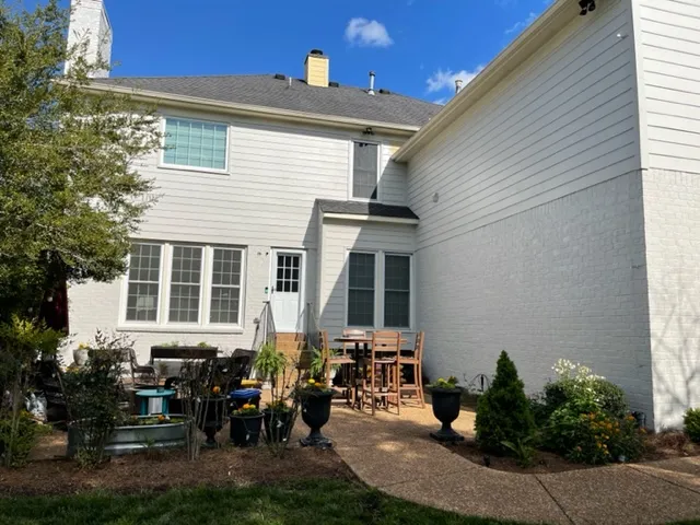 The back of the Allison house before the porch: a small concrete patio with a table and potted plants against painted brick