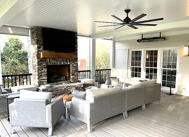 The finished Allison porch: a stone fireplace with a television, a wall heater, a ceiling fan over the composite floor, and French doors to the house