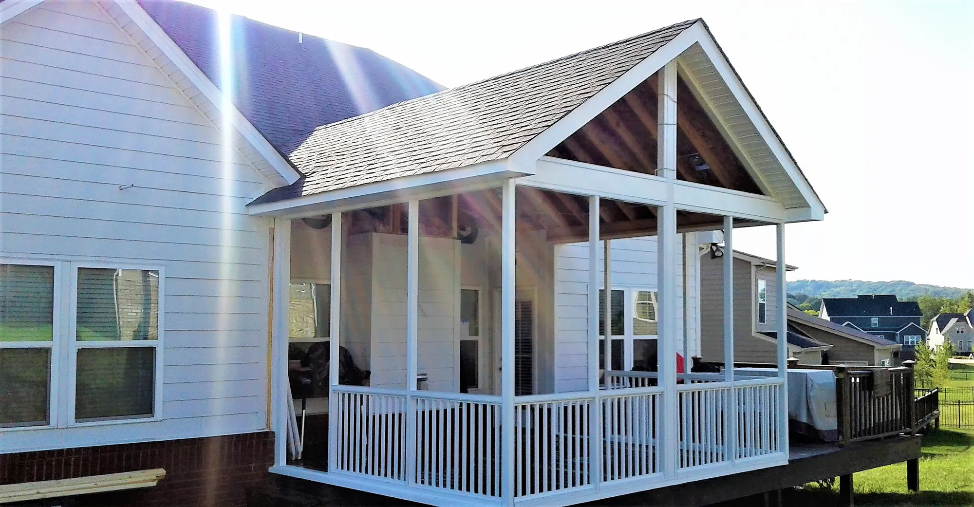 White aluminum screen room with a gable roof and white railing on a raised deck beside gray siding