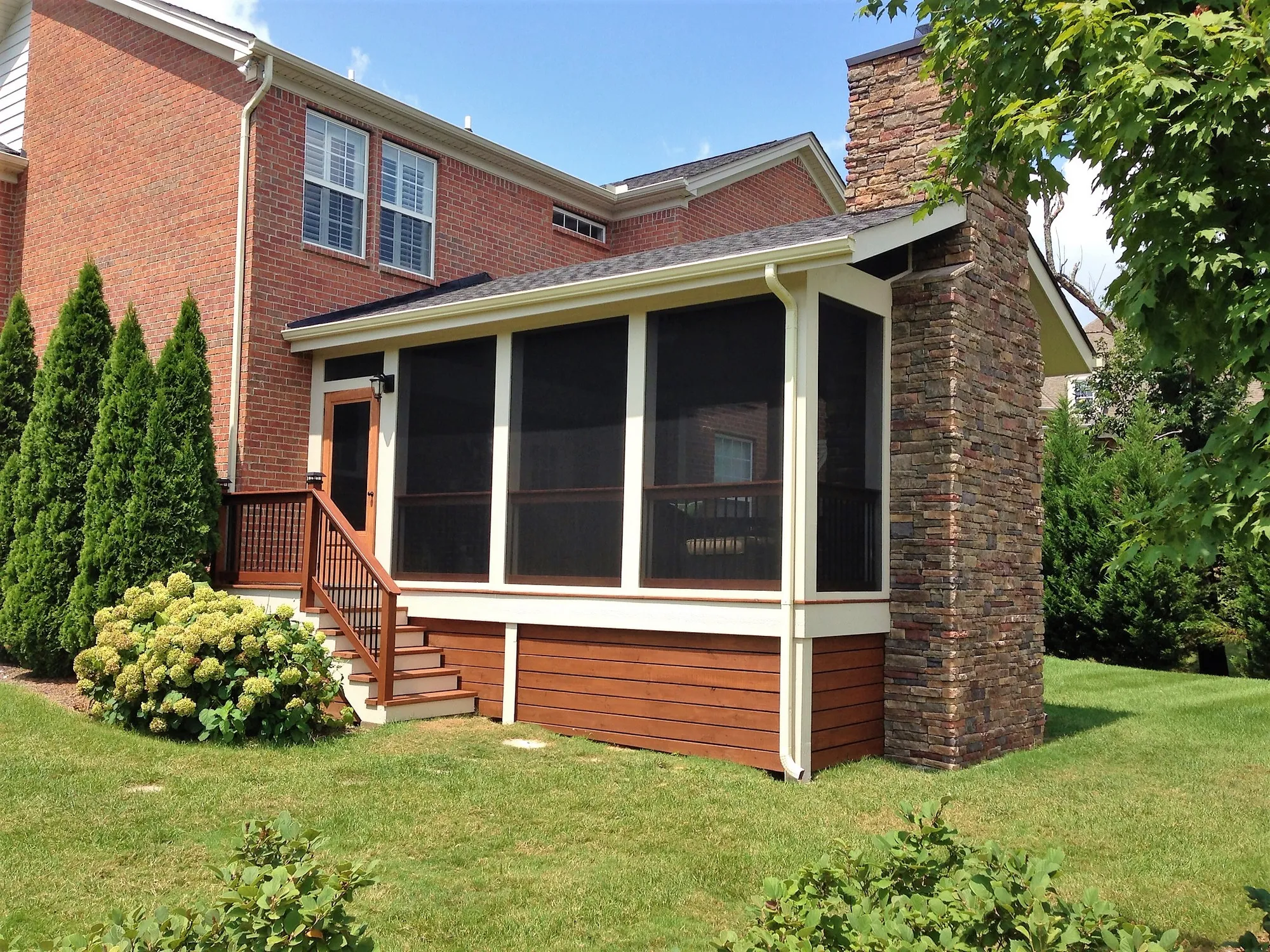 The same brick house with a screen room and a tall stone chimney where the deck was