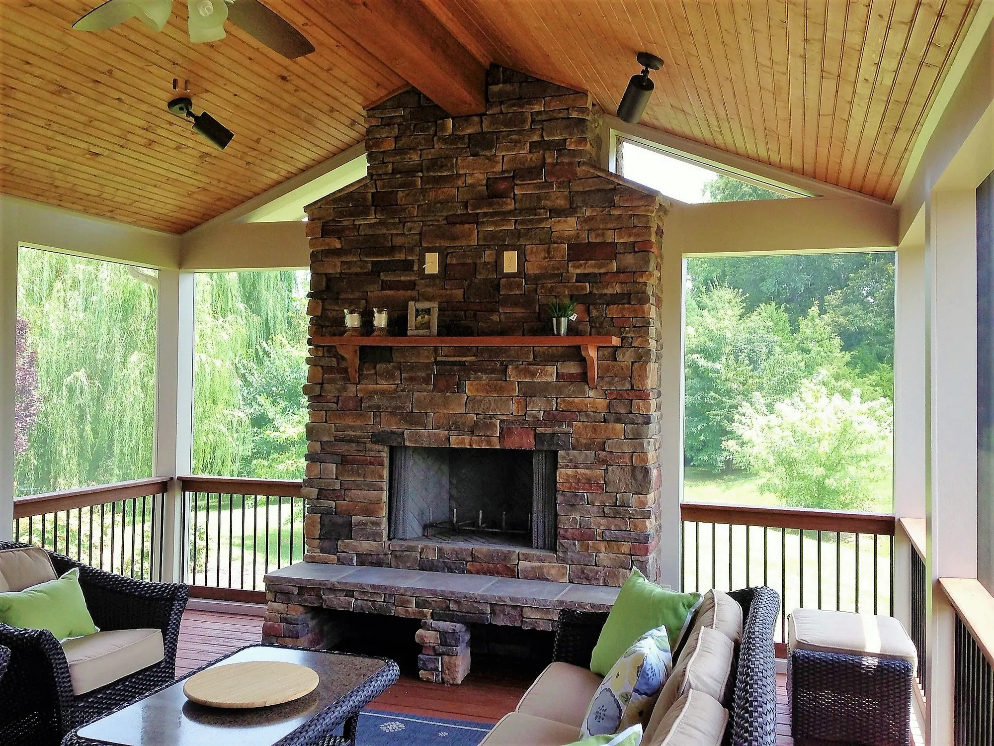 Inside the new screen room: a stacked stone fireplace with a log mantel under a vaulted wood ceiling