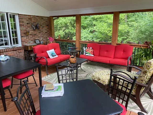 Corner of the cedar screen room with cedar posts, red cushioned sofas and a dining table, trees beyond the screens