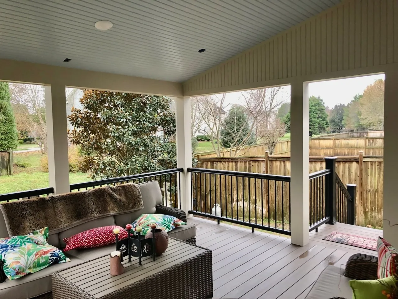 Covered deck with white columns, black railing and a cushioned outdoor sofa