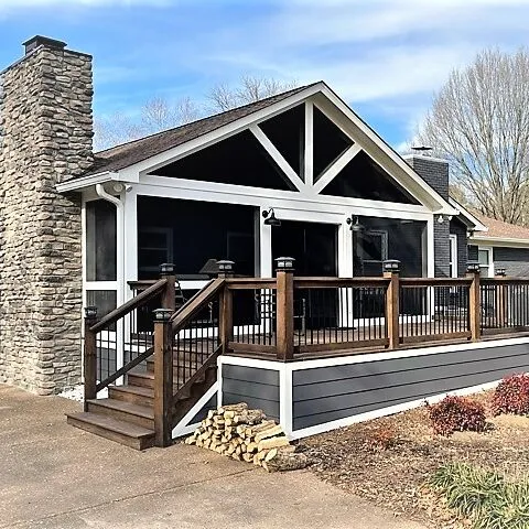 Gable screen room with a stone chimney on a gray deck with dark stair railing