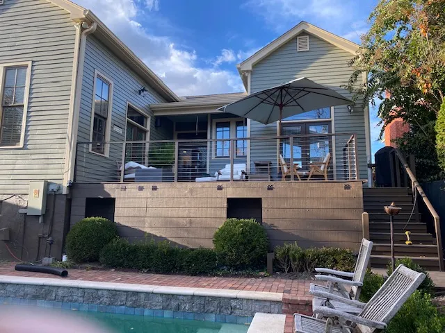 Raised deck with cable railing above a pool and brick pool deck, with an umbrella and chairs