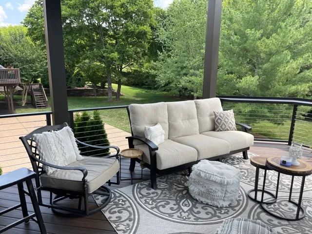 Deck with black cable railing, a cream outdoor sofa and swivel chairs around a pouf on a patterned rug