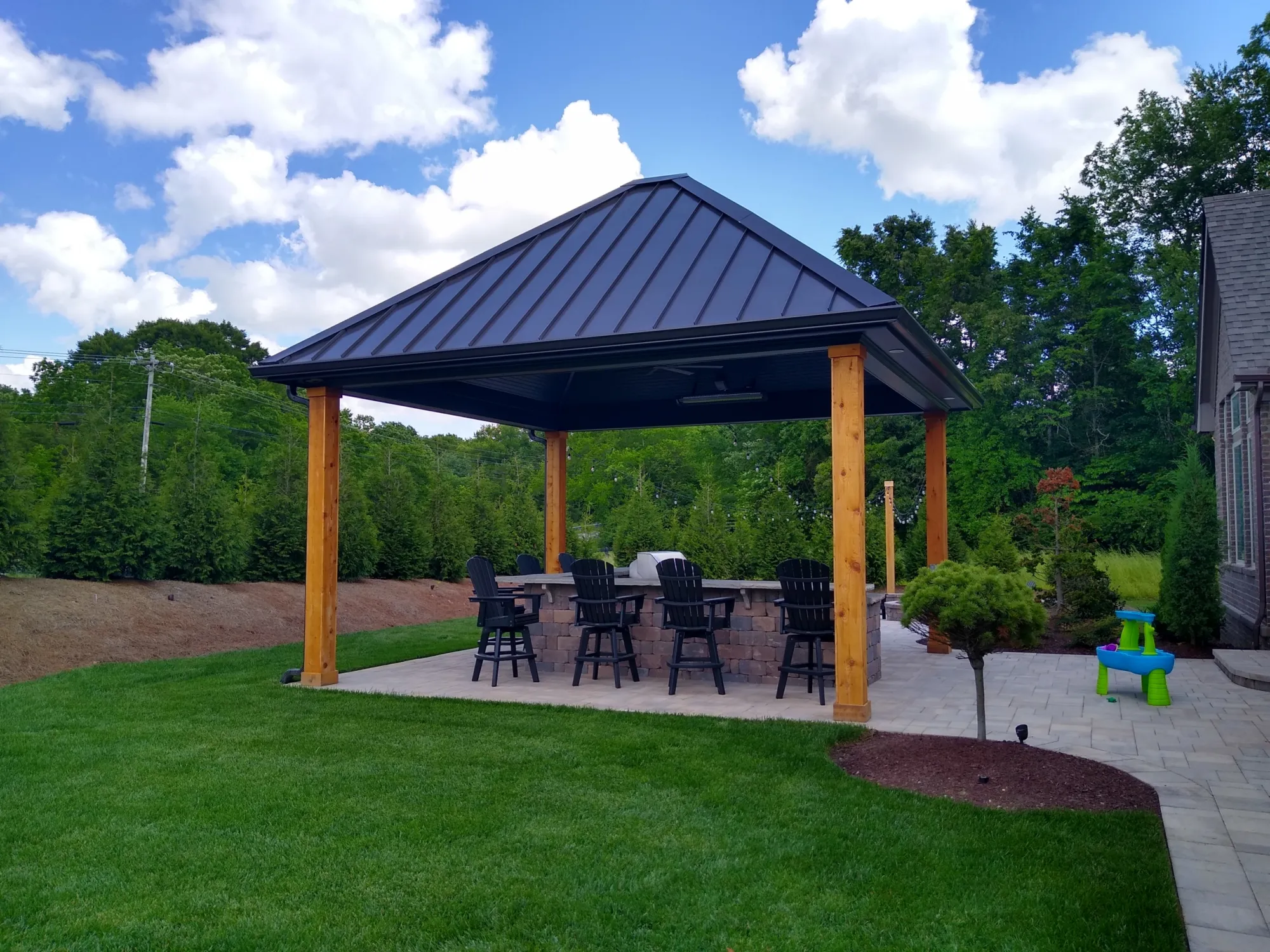 Freestanding pavilion with a dark standing seam roof on stained wood posts over a patio bar in a Franklin back yard