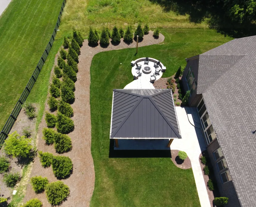 Aerial view of the Franklin pavilion roof in a long back yard lined with evergreens, the fire pit circle beyond it