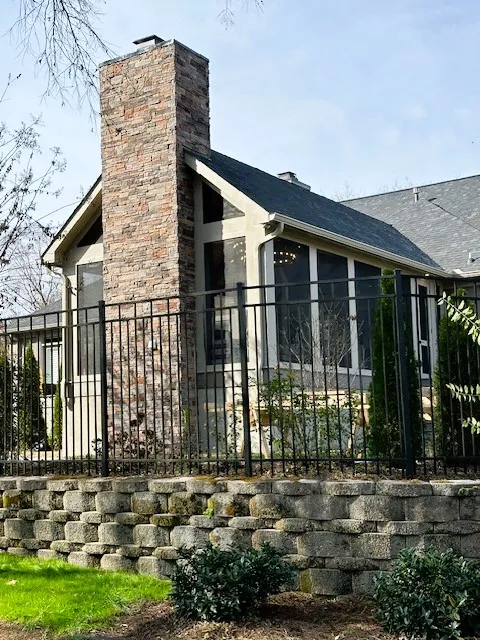 Gable screen room seen from the yard behind an iron fence, with a tall stone chimney on its end wall