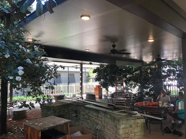 Insulated roof with lights and fans over a stone outdoor kitchen bar and dining area in Belle Meade