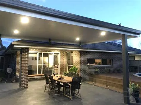 Insulated patio cover with recessed lights on a dark post over a dining table outside a brick house
