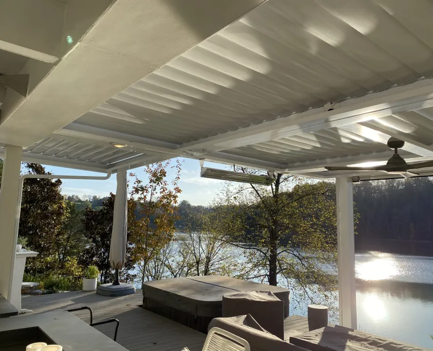 White louvered roof with ceiling fans over a covered patio looking out on a lake