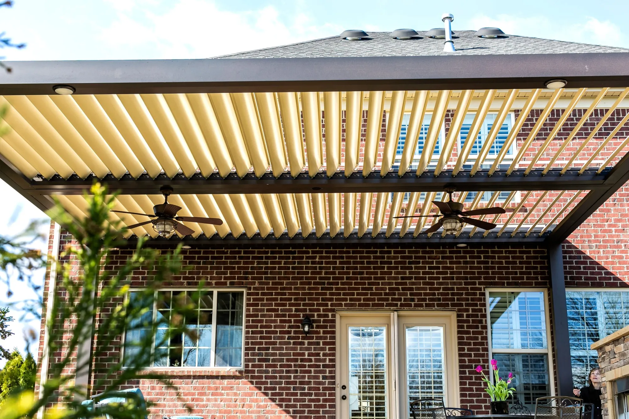 Louvered roof with its blades open over a brick patio and ceiling fans