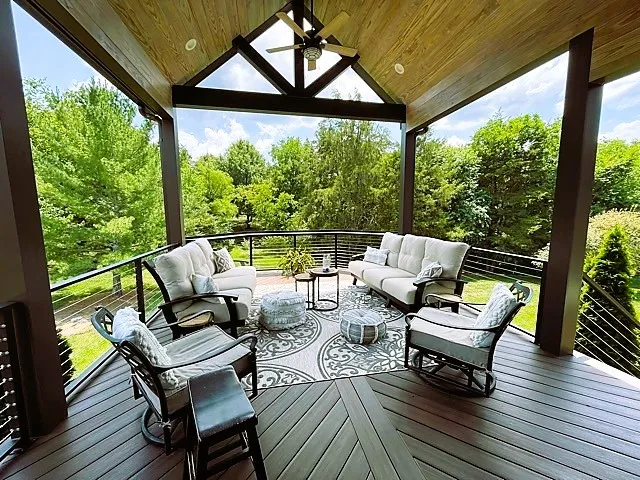 Open gable roof with a wood ceiling over a deck with cable railing, swivel chairs and a round outdoor rug