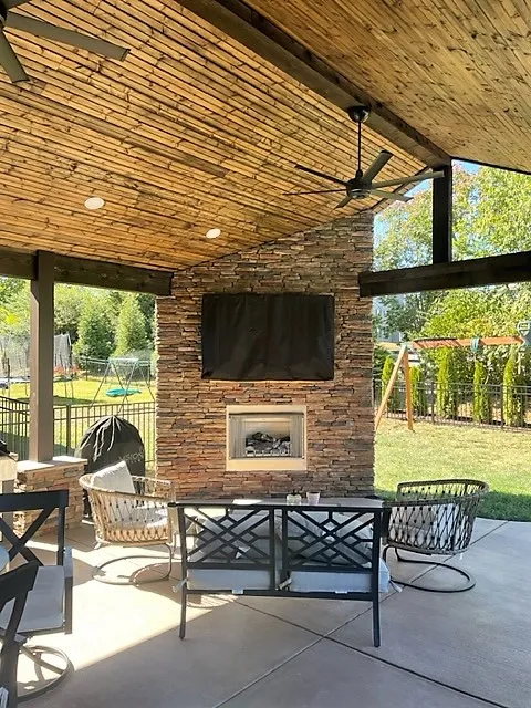 Open roof with a wood plank ceiling and ceiling fan over a patio, a stone fireplace and a television