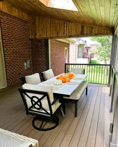 Open roof with a wood plank ceiling over a dining table beside a brick wall