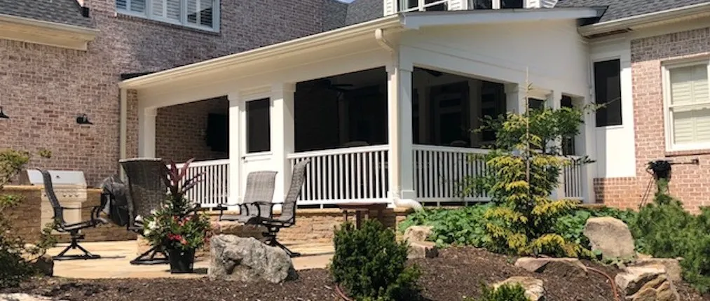 Open porch roof with white columns and white railing across the back of a brick house