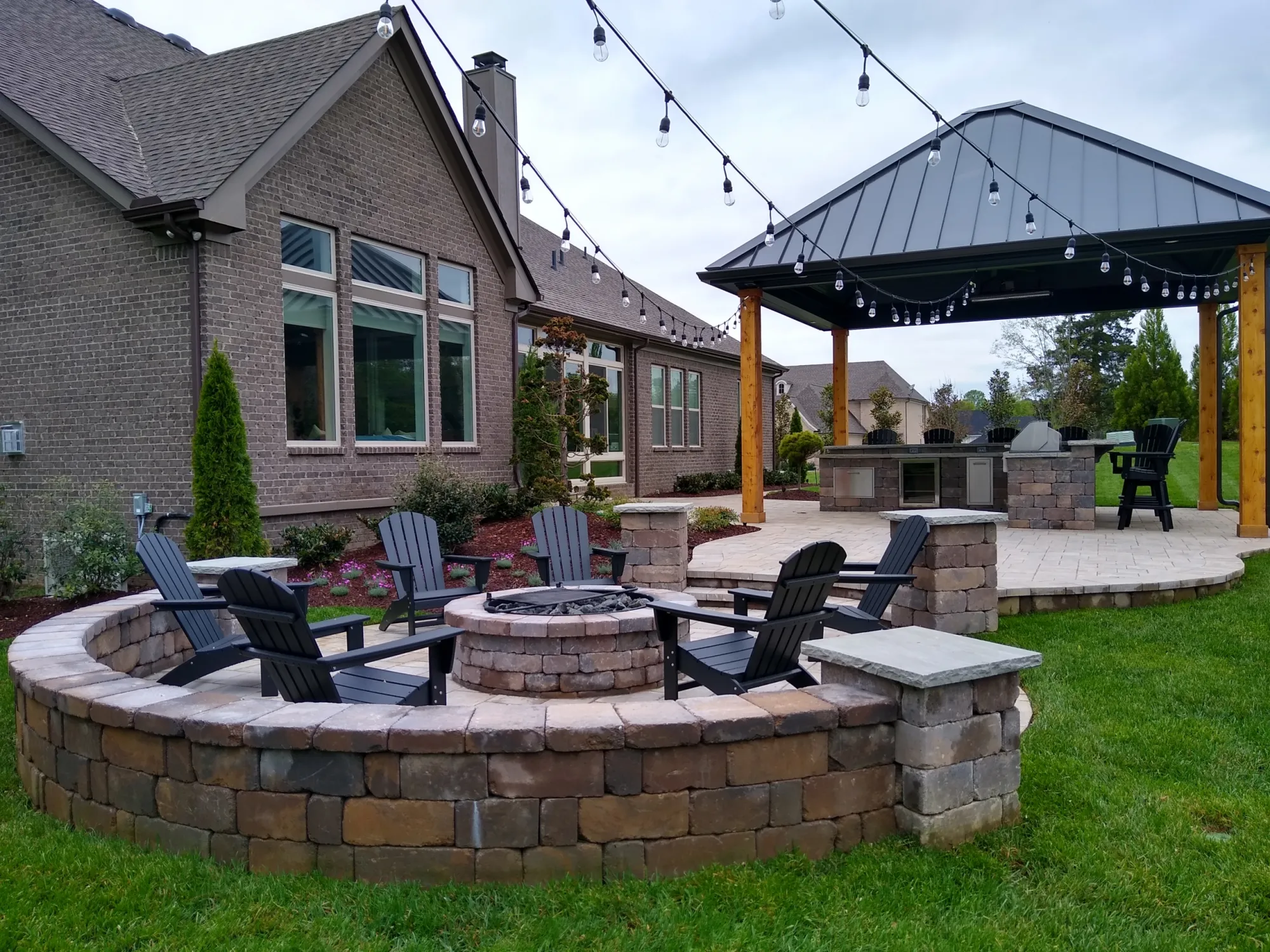 Pavilion roof over an outdoor kitchen with a stone fire pit and chairs in front