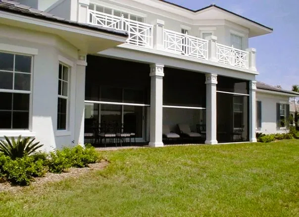 Dark power shades lowered between the white columns of a covered porch beneath a second-floor balcony