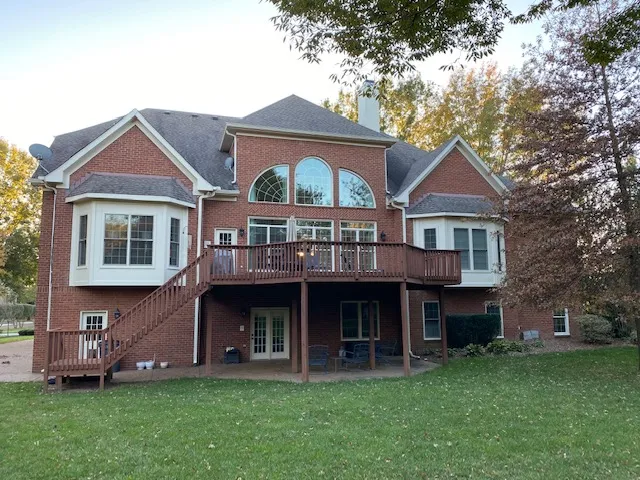 Back of a red brick house with a raised wood deck and long wood stairs down to the lawn