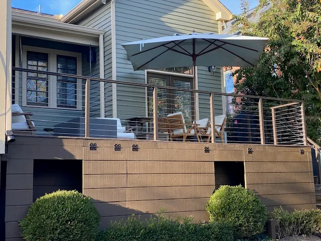 Raised composite deck with cable railing and a patio umbrella, its skirt finished in matching boards