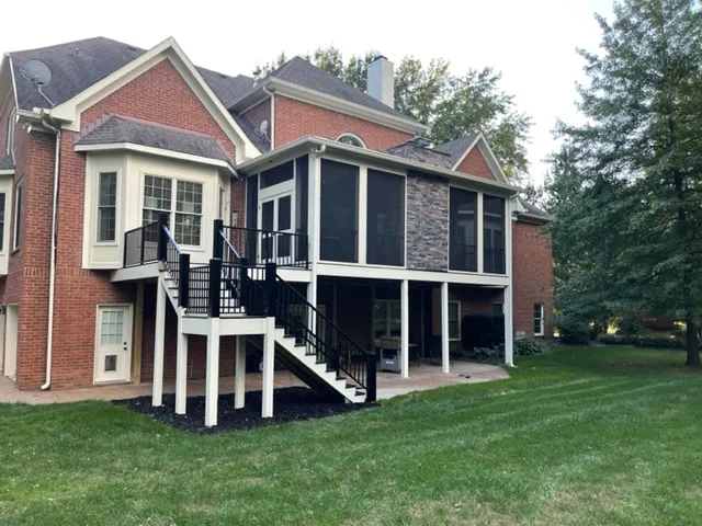 The same brick house with a screen room on the raised deck, a stone chimney and black stairs to the lawn