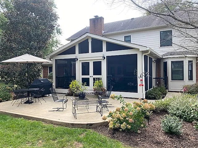 Gable screen room with white trim and French doors seen from the lawn, a patio and umbrella beside it