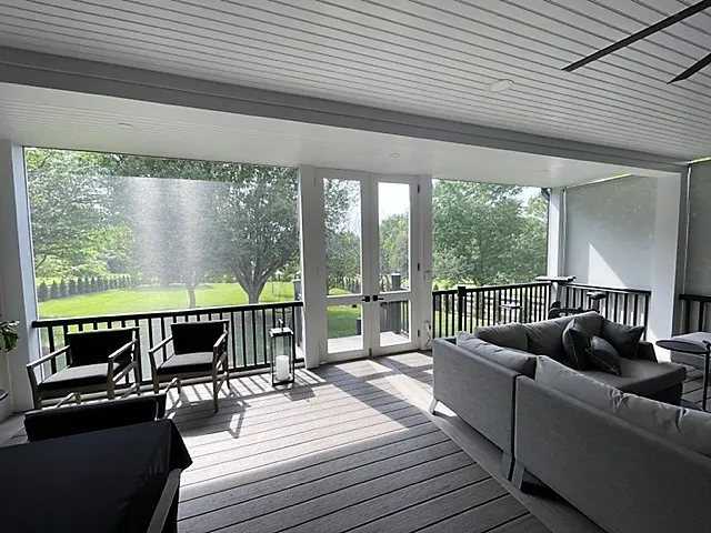 Screen room with a gray sectional and black railing looking across a wide lawn