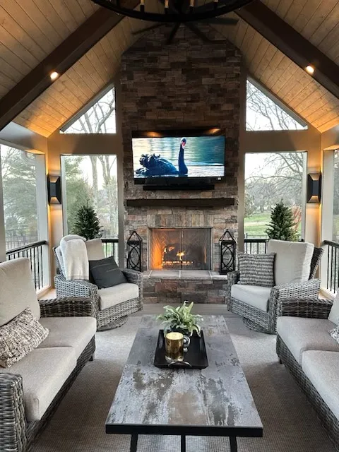 Screen room with a stone fireplace, a television above it and heaters on the beams