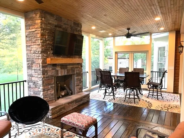 Screen room with a stacked stone fireplace, a television on it, a wood ceiling with recessed lights and a dining set