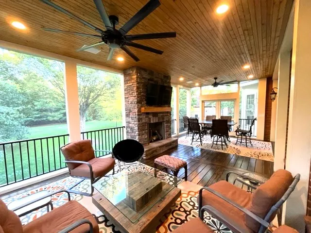 Screen room with a wood ceiling, a black ceiling fan and a brick fireplace beyond the seating