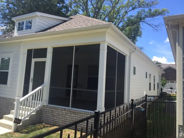 Screen room built under the main roof of a white house, with dark screen panels and white steps to the yard
