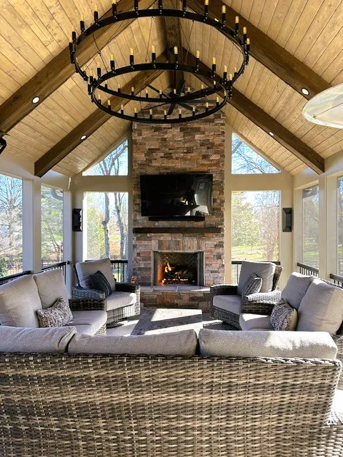 Inside the Turtle Creek screen room: a vaulted wood ceiling, a round iron chandelier, wicker seating and a stone fireplace