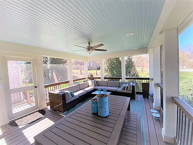 Screen room with a white beadboard ceiling, a ceiling fan and dark wicker seating on a composite floor