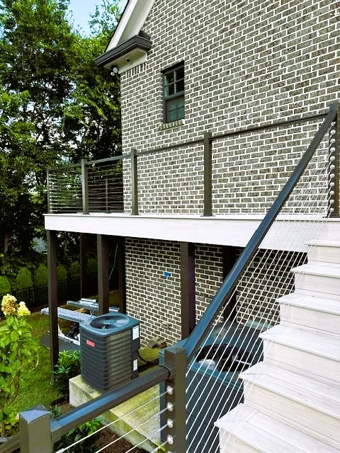 Second-story deck on the side of a gray brick house with cable railing and white stairs going down
