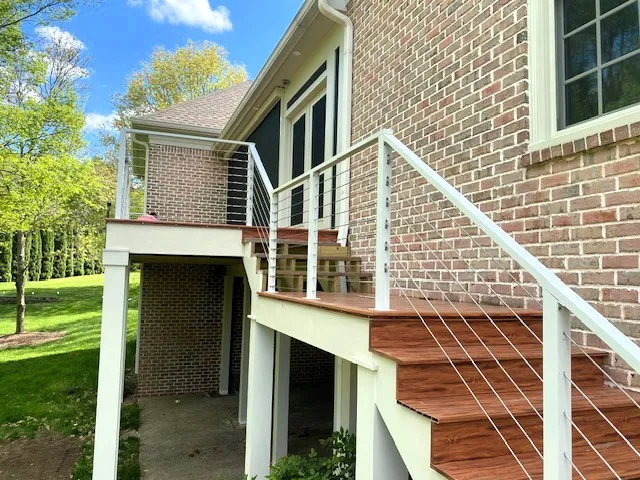 Wood deck stairs with white posts and cable railing against a brick house