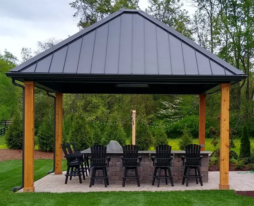 Dark standing seam metal pavilion roof on stained wood posts over a stone bar with black bar chairs