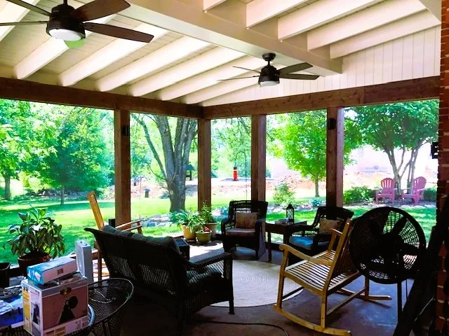 Screen room under a shed roof with white exposed rafters, rocking chairs and a view of the trees