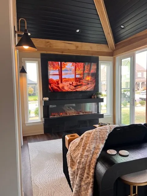 Sunroom corner with a linear electric fireplace under a television and a dark tongue-and-groove ceiling