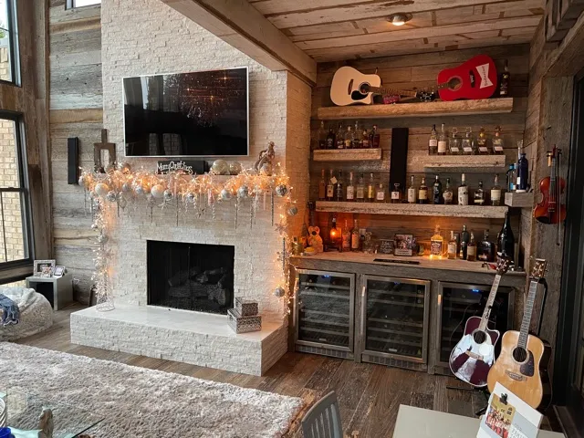 Whitewashed brick fireplace with a television above and a bar of shelves and wine coolers beside it, inside a sunroom