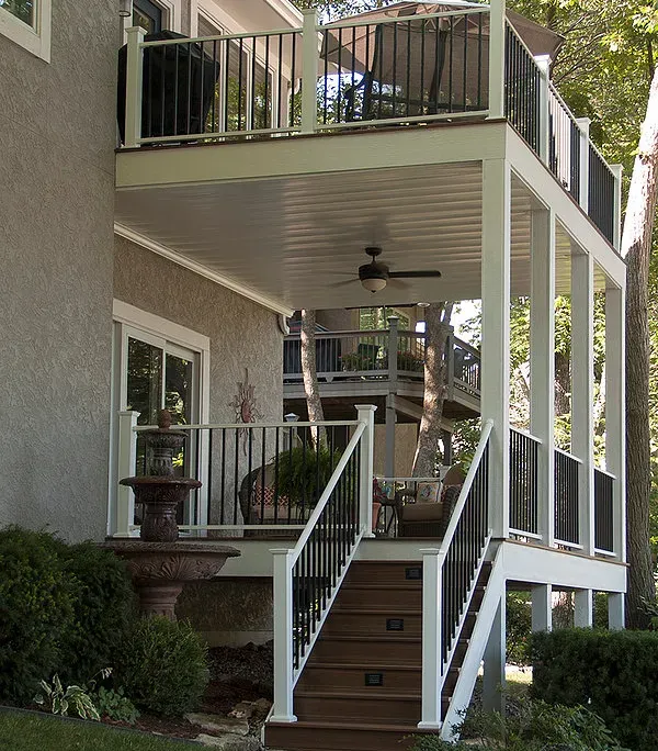Covered patio under a second-story deck with a white ceiling, a ceiling fan, black railing and white stairs