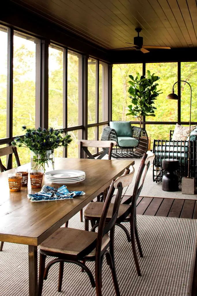 Upper-level screened porch with a wood dining table, a ceiling fan and dark screen frames looking into trees