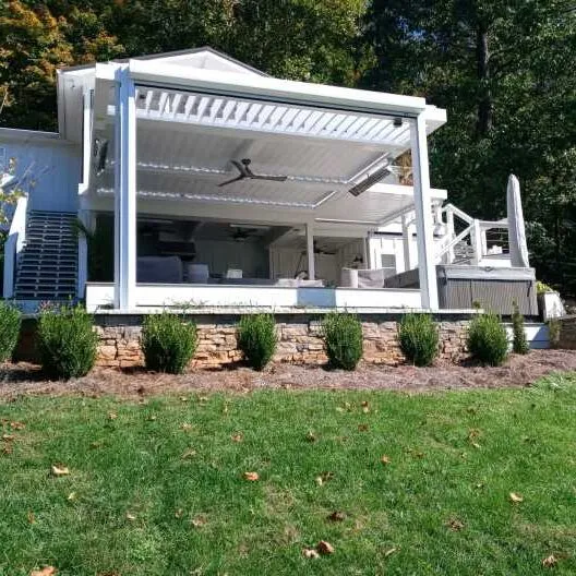 White louvered roof over a raised porch on a stone base, with shrubs along the front