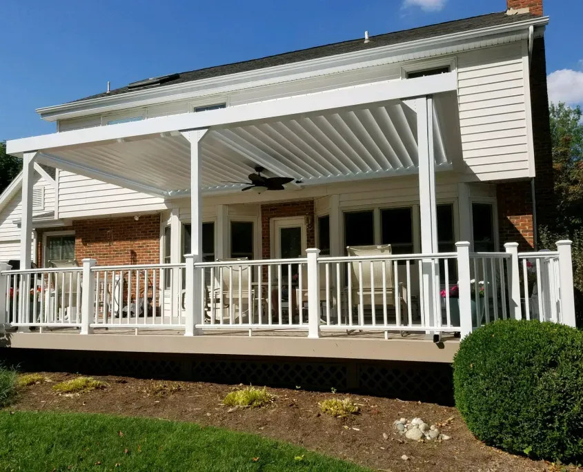 White railing around a deck under a white louvered roof on the back of a brick house