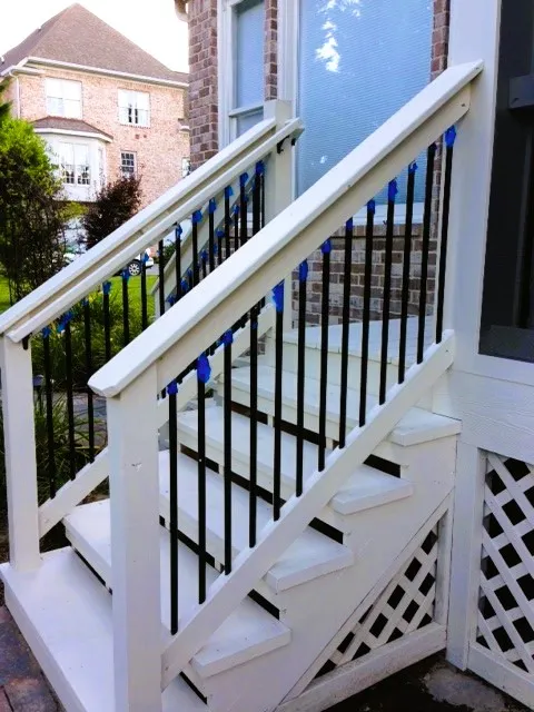 White stair railing with black metal balusters running down beside a white lattice skirt